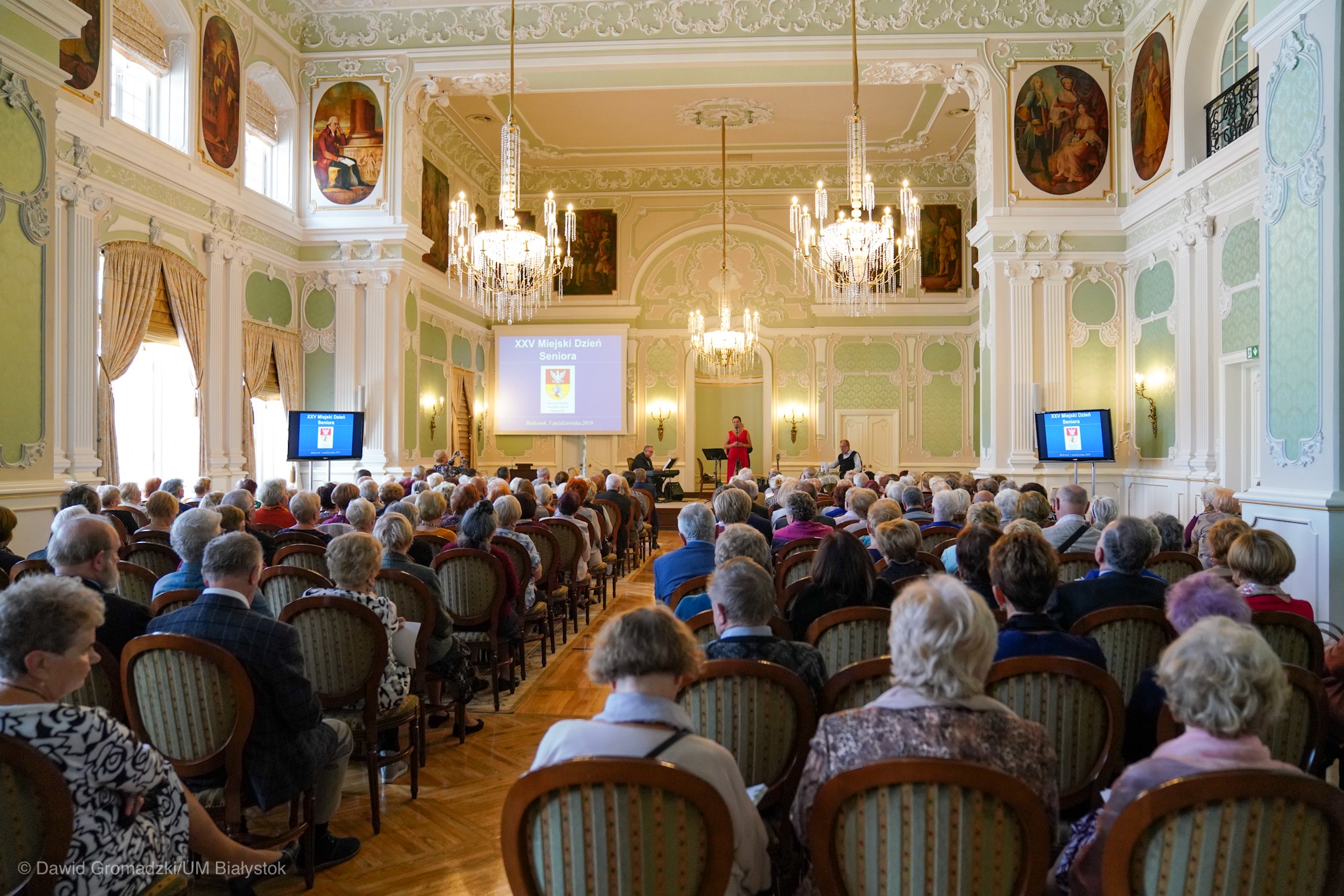 Sala w pałacu Branickich wypełniona siedzącymi osobami starszymi słuchającymi koncertu